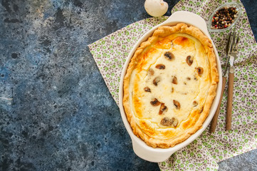 Homemade delicious quiche with mushrooms and cheese in a dish on a blue stone background.