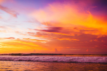Ocean with waves at colorful bright sunset with clouds