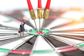 Miniature people: businessman standing on dartboard target center with arrows idea of financial and business goal