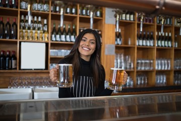 Smiling waitress holding glass of beer at counter