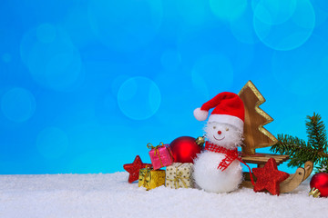 Snowman with Christmas gifts on the sledge isolated on blue winter background.