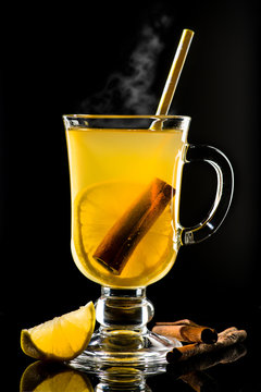 Hot grog with lemon, cinnamom stick and honey with steam on dark background