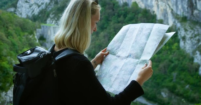 Beautiful Blonde Female Hiker Looks at the Map While Standing on the Mountain Trail