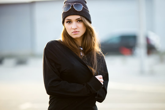 Outdoor fashion closeup portrait of nice pretty young hipster woman posing in sunglasses at sunset walks along the streets of the city.