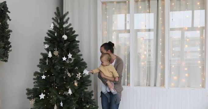Christmas concept. Little baby boy with mother in sweater decorates the Christmas tree. Year-old child waiting New Year , happy family concept