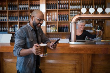 Man using mobile phone while having glass of beer in bar