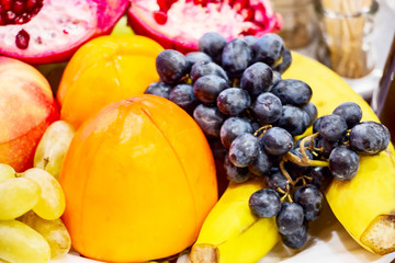 Still life. Fruit in a plate on the table. Pomegranates, apples , bananas, grapes and persimmons