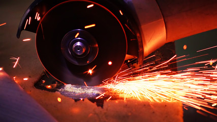 Cutting metal with disc grinder abrasive saw producing bright colorful sparks. Worker cuts metal with hand electric tool.
