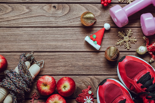 Fitness, healthy and active lifestyles love concept, dumbbells, sport shoes, skipping rope or jump rope and apples with Christmas decoration items on wood background. 