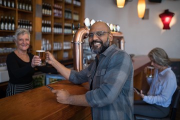 Senior waitress serving glass of beer to customer at counter