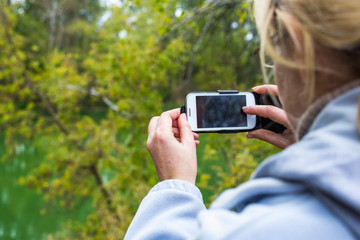 A blonde woman using a phone takes a photo of a beautiful landscape