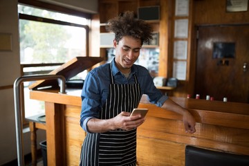 Smiling waiter using mobile phone at counter - Powered by Adobe