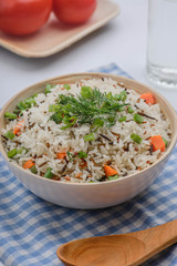 boiled mix rice in a white bowl on the white table with a wood spoon