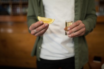 Man holding tequila shot and lemon wedge in bar