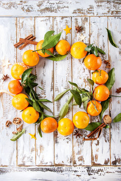 Clementines tangerines with leaves as Christmas wreath with cinnamon sticks and anise over white wooden plank background. Top view, space. New Year cards and decorations.