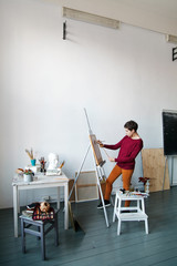 Female artist in her spacious white studio working with watercolor painting.  Natural lighting. Disclosure of creativity concept. Vertical composition with copy space
