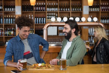 Two male friends having glass of beer and mexican food in bar