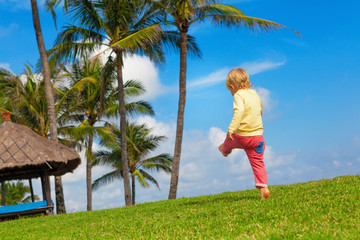 Happy child have fun at outside walk without parents. Active boy run and jump high by grass lawn in luxury resort garden. People activity on summer tropic holiday with kid. Family lifestyle background
