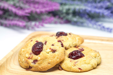 Cranberry cookies on wooden plate with blurred pink and violet flowers background