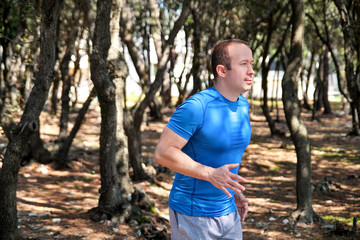 Obraz premium Running man jogging for fitness running in landscape nature outdoors. Handsome young sportsman wearing sportswear and running and exercises in forest. Pretty guy, active, cross fit, healthy lifestyle.