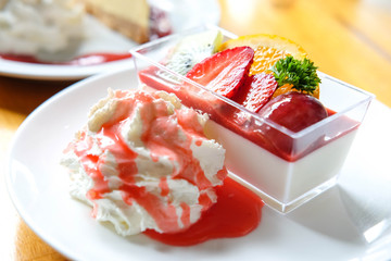 Yogurt pudding with fresh fruit and strawberry sauce on top and wipping cream on white plate on wooden desk in the morning time