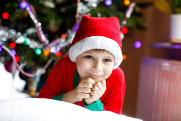 Little kid boy in santa hat with Christmas tree and lights on background.