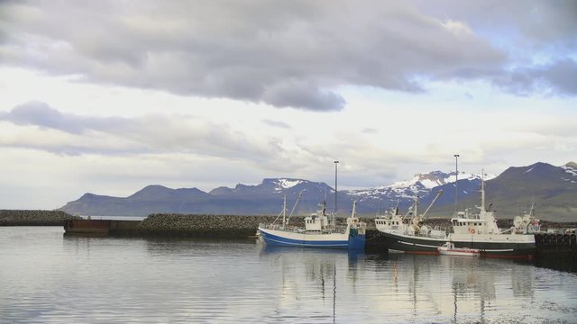 Northern harbor port with fishing and whale watching boats and little ships and snow mountains with moving clouds at sunset