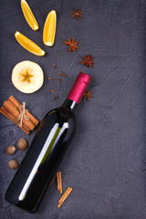 Bottle of red wine and mulled wine ingredients on black background. Spices and fruits for hot alcohol drink, copy space, top view, vertical