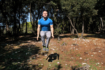 Man doing workout jump up in air exercise in forest. Handsome sportsman wearing sportswear is jumping up in air exercise in beautiful landscape nature outdoors. Cross fit, healthy lifestyle concept.