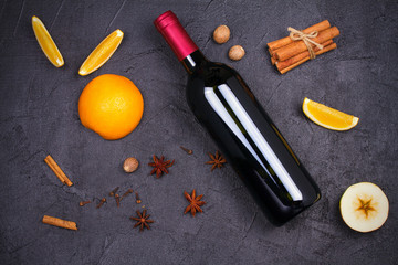 Fototapeta na wymiar Bottle of red wine and mulled wine ingredients on black background. Spices and fruits for hot alcohol drink, copy space, top view, horizontal