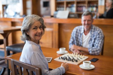 Man and woman looking at camera while playing chess