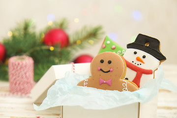 Christmas cookies in a box with gifts, lights and fir branches on white vintage wooden table. Snow effect, bokeh