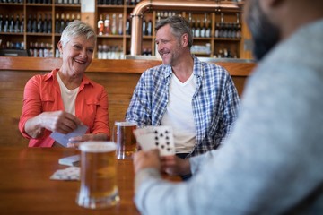 Happy friends playing cards while having glass of beer