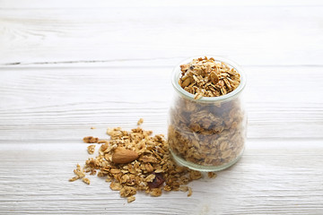 Granola superfood with almond and cashew nuts, dry fruits, raisins cherry in the glass jar on the white wooden table, top view, bright light