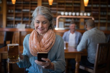 Smiling senior woman using mobile phone while having glass of