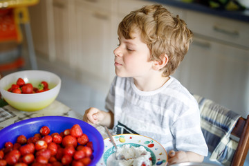 Little blond kid boy helping and making strawberry jam in summer