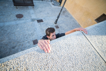 Young man hanging on wall on hands and trying to climb up while doing parkour.  