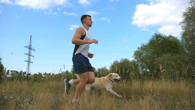 Young man running outdoor with his dog. Labrador or golden retriever jogging with his male owner at nature. Healthy active lifestyle. Slow motion Side view
