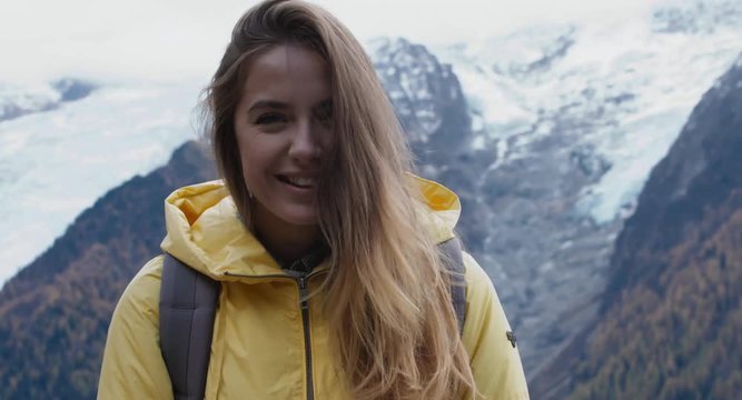 Beautiful Caucasian female hipster hiker making a selfie or video call in front of Mont Blanc massif. 4K UHD RAW 60 FPS SLO MO