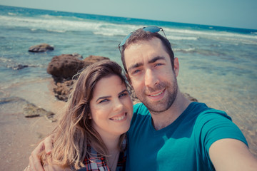 Young couple taking selfie with smartphone or camera at the beach