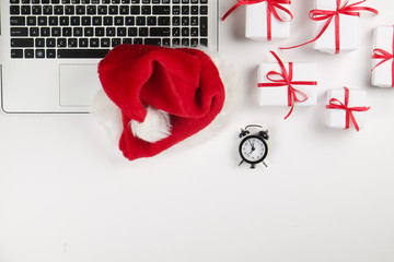 Office desk with laptop, christmas presents, cup of coffe and santa hat on white background flat lay with copy space. Business christmas holidays concept, holiday online shopping concept