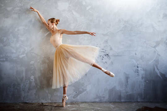 Young ballerina in a golden colored dancing costume is posing in a loft studio