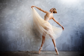 Young ballerina in a golden colored dancing costume is posing in a loft studio - obrazy, fototapety, plakaty