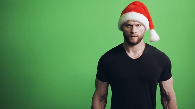Sportsman in Santa Claus hat pumping bicep on green background