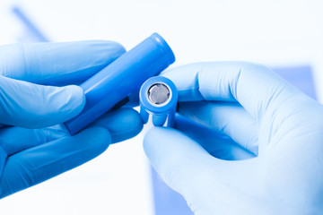 Scientist hold in hand in protective gloves small accumulator battery, new type of rechargeable...