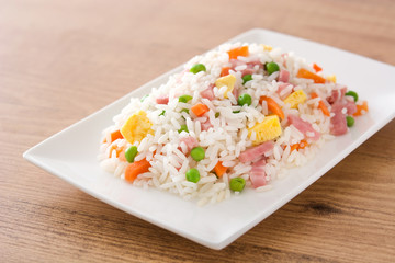 Chinese fried rice with vegetables and omelette on wooden table.