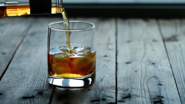 Pouring a scotch whiskey into glass with ice
