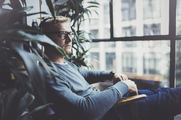 Attractive young man wearing glasses casual clothes.Man sitting in vintage armchair modern loft studio and relaxing whith headphone music. Blurred background.Horizontal.