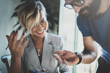 Coworkers working process at home.Young blonde woman working together with bearded colleague man at modern home office.People making conversation together.Blurred background.Horizontal.
