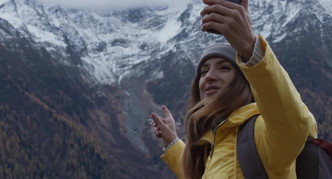 CRANE SHOT Beautiful Caucasian female hipster hiker making a selfie or video call in front of Mont Blanc massif. 4K UHD RAW 60 FPS SLO MO